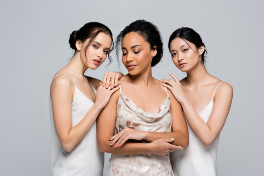 Interracial women in satin dresses posing isolated on grey