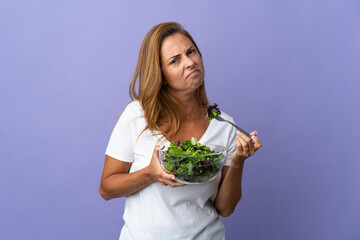 Middle age brazilian woman isolated on purple background holding a bowl of salad with sad expression