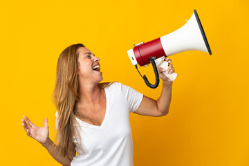 Middle age brazilian woman isolated on yellow background shouting through a megaphone to announce something in lateral position