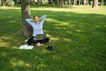 Side view of happy smiling woman sitting in a park on green grass with a laptop, outdoor worker, remote work.