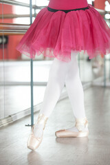 Legs of a dancing ballerina in a training hall with mirrors. Cream pointe shoes and a bright crimson tutu skirt