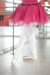 Legs of a dancing ballerina in a training hall with mirrors. Cream pointe shoes and a bright crimson tutu skirt