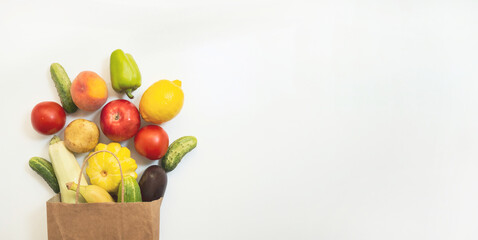 A paper shopping bag with vegetables and fruits, tomato, cucumber, squash, pepper, lemon, eggplant, zucchini, banana, apple, peach on white background