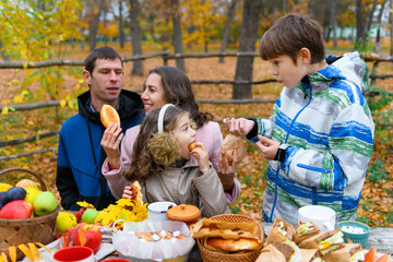Happy family portrait in autumn city park. People are sitting at the table, eating and talking. Posing against the background of beautiful yellow trees. They are happy together.