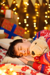 Portrait of teenage boy sleeping in new year or christmas decoration. Holiday lights, gifts and christmas tree decorated with toys.