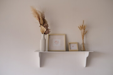 White shelf with easels and dry flowers and mock up frames with drawings