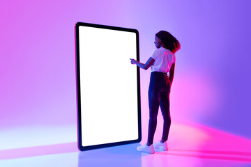 Millennial black woman touching screen of huge tablet computer, interacting with pc interface in...