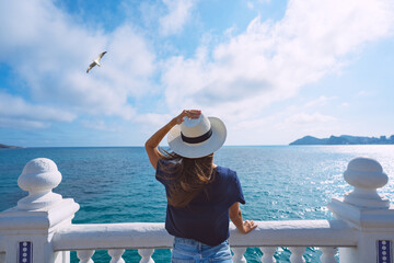 Rear view of woman tourist with sun hat enjoying sea or ocean view. Summer holiday vacation