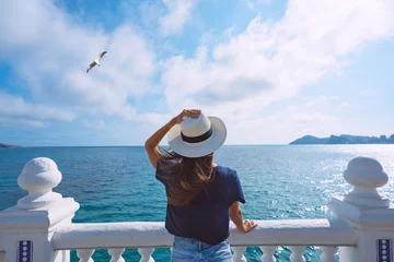 Fototapete Blauer Himmel Rear view of woman tourist with sun hat enjoying sea or ocean view. Summer holiday vacation