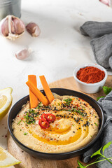 Delicious hummus in ceramic bow lwith  carrot stick dipped in hummus. Colorful snack composition on a white background.