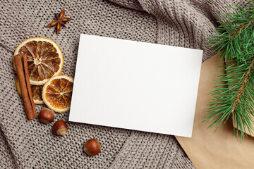 Christmas greeting card mockup with dry oranges, nuts, spices and cone tree branches on knitted background