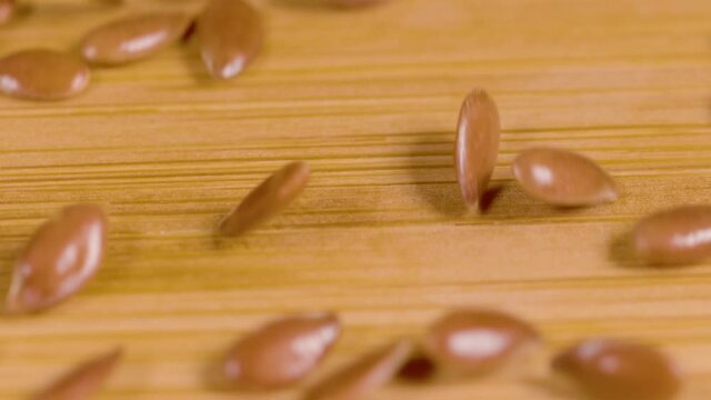 SLOW MOTION, MACRO, DOF: Linseeds glide along the wooden surface inside a packaging facility. Reddish brown hued flaxseeds slide down a wooden kitchen countertop. Tiny seeds get scattered across board