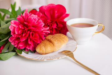 Cup of tea and croissant with hydrangea flowers on white table