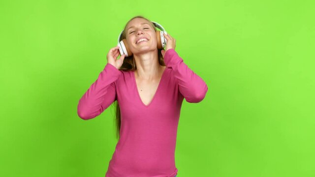 Young blonde girl listening to music with headphones over isolated background. Green screen chroma key