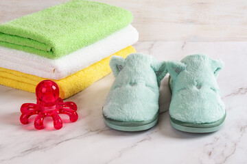 Obraz na płótnie Canvas Red spa massager and funny cozy slippers near stack of colored terry towels over marble surface. Massage tool, warm home shoes and cotton toiletries for hygiene and relaxation concepts.