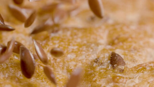 SLOW MOTION, MACRO, DOF: Seeds are scattered across the crust of a loaf of delicious whole-wheat bread. Detailed close up shot of the crispy crust of an unleavened bread sitting on the dining table.