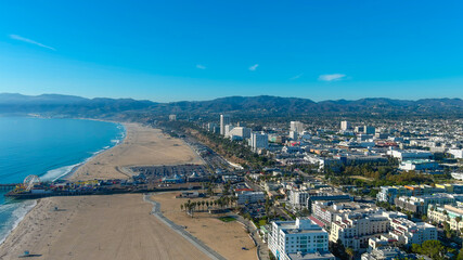 a stunning aerial shot of the coastline with silky brown sand, vast blue ocean water, a long wooden...
