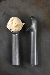 High angle shot of two old fashioned metal ice cream scoops one with a scoop of vanilla.