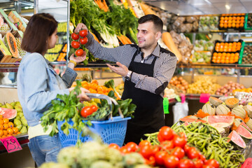 Male shopping assistant helping customer to buy fruit and vegetables in grocery shop