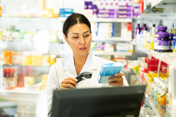 Portrait of female pharmacist working at the cash register in pharmacy - scans barcode on the medicine package