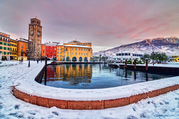 Beautiful view of Riva del Garda on a winter day with lots of snow, View of the beautiful Lake Garda in a snowy day surrounded by mountains, Trentino Alto Adige region - obrazy, fototapety, plakaty