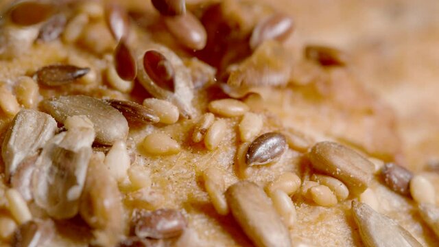 SLOW MOTION, MACRO, DOF: Reddish brown hued linseeds fall on the crust of a homemade rustic unleavened bread. Cinematic shot of seeds being scattered across a loaf of delicious whole-wheat bread.