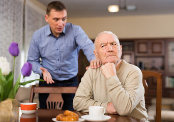 Adult son trying to apologize to offended elderly father after quarrel at home..