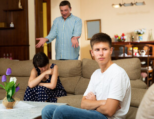 Obraz na płótnie Canvas Unhappy young guy sitting on sofa during his parents quarrelling