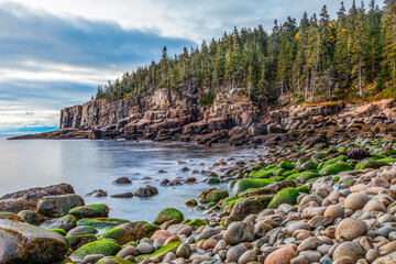 The glow of just before sunrise illuminates the rounded stones on Boulder Beach and the steep rock walls of the Otter Cliffs rising from the sea in Acadia National Park on Mt. Desert Island, Maine.