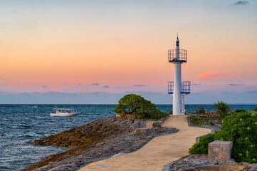 A small lighthouse in Onna Son, Okinawa, Japan, marks the edge of an artificial island and jetty that surround a beach and marina. Seen at sunset