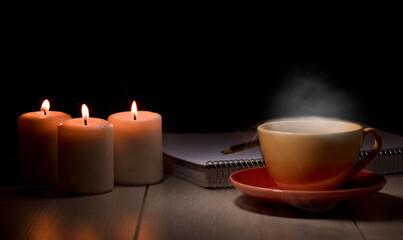 table with burning candles notebook pencil books, yellow mug with steam smoke