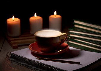 table with burning candles pencil notebook, yellow mug with smoke steam