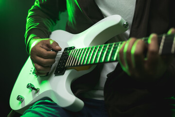 Close up hands young man rocker playing electric guitar on stage live in concert. With neon light....