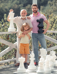 Grandfather with son and grandson playing chess. Amazed men in different ages playing chess board...