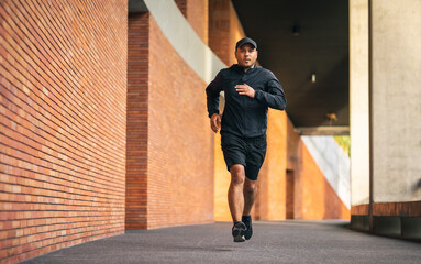 Asia man wearing jacket sportswear running on the road under the building. Young man jogging for...