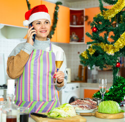 Smiling adult woman preparing for holidays celebration and using phone at kitchen decorated for Christmas