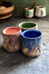Colorful clay mugs on a kitchen counter created by hand on a pottery spinning wheel.