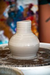 Pottery on a spinning wheel with a colorful background. The clay jug has texture from fingers creating it.