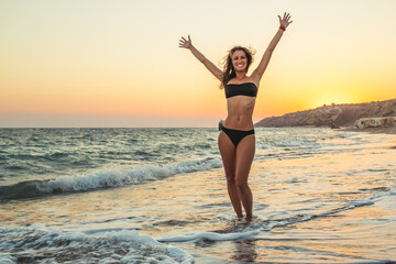Fototapeta na wymiar Young woman in bikini with raised hands and feel freedom at the beach
