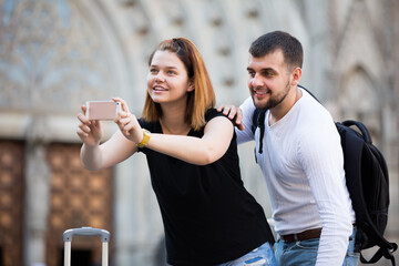 . positive tourists standing with baggage at street and taking selfie