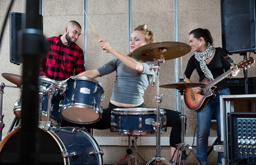 Fototapeta na wymiar Rehearsal of a music group. Rock band with emotional female drummer playing in recording studio