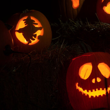 carved Halloween pumpkins in shapes of a witch flying on a broom stick the other a scary face both lit by candle light on a dark night representing all Hallows eve pumpkins glowing horizontal format 