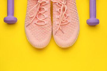 Fototapeta na wymiar Dumbbells and shoes on yellow background