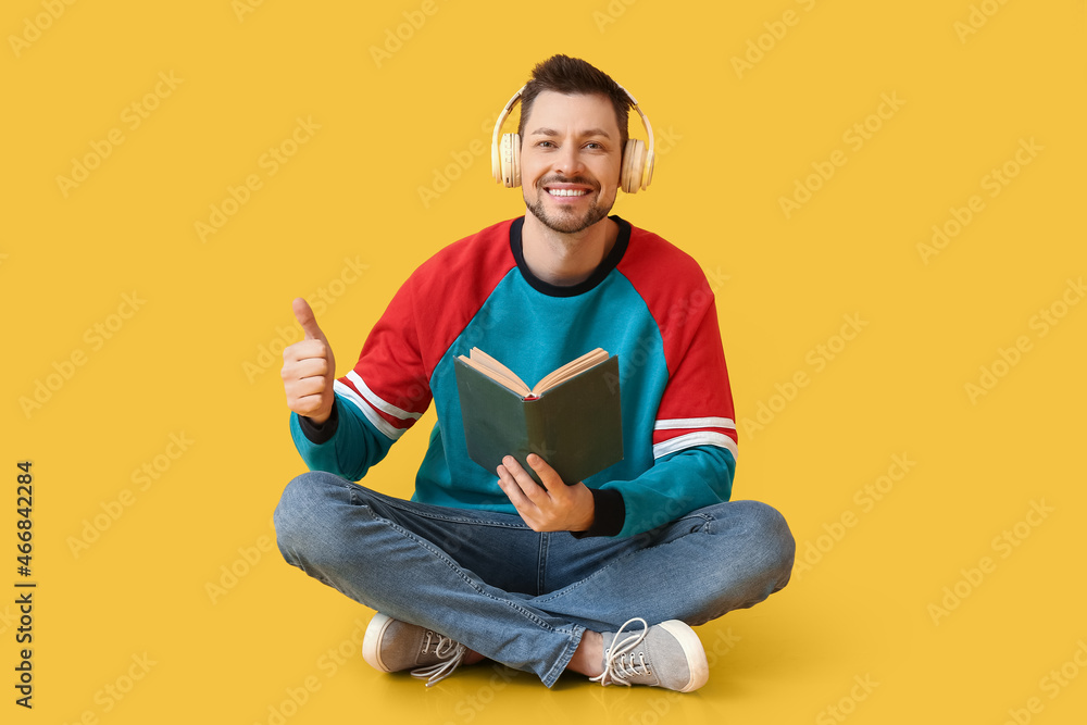 Poster man with headphones and book showing thumb-up on color background