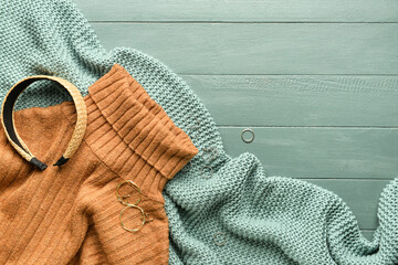 Knitted plaid, warm sweater and female accessories on color wooden background