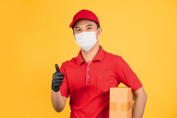Fototapeta na wymiar Delivery man in red uniform He was wearing a mask and black gloves holding a brown cardboard box and thumbs up.