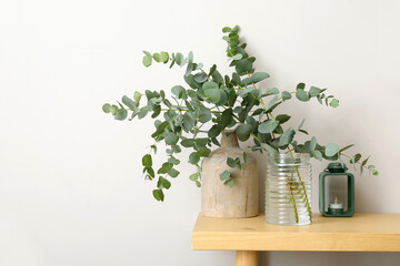 Vases with green eucalyptus branches on table near light wall