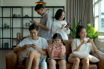 Multi-generation Asian family sitting on sofa and using mobile phone, laptop and digital tablet,...