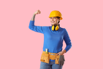 Female construction worker with hardhat and ear protectors on pink background