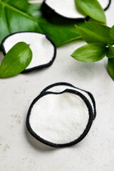 Reusable cotton pads and green leaves on light background